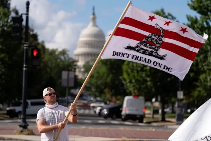 A demonstrator waves a flag protesting against President Donald Trump's use of federal law enforcement and National Guard troops in the city during protest at the U.S. Capitol, Tuesday, Sept. 2, 2025, in Washington