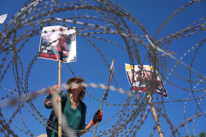 A woman places pictures of hostages Nimrod Cohen, left, and Eitan Horn, held in Hamas captive in the Gaza Strip , on a barbed wire during a protest by families at the plaza known as the hostages square in Tel Aviv, Israel, Saturday, Aug. 2, 2025. ( AP Photo/Ariel Schalit)