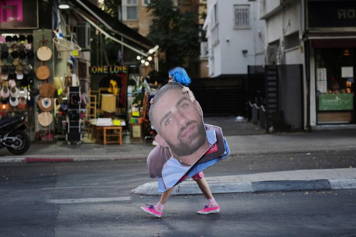 A demonstrator carries a photo of Israeli hostage Segev Kalfon who is held in the Gaza Strip, during a protest demanding the release of all hostages from Hamas captivity and calling for an end to the war, in Tel Aviv, Israel, Thursday, Aug. 7, 2025. (AP Photo/Ariel Schalit)