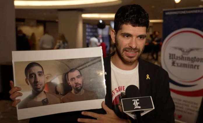 Ilay David holds up a screen grab from a Hamas propaganda video showing his brother, Evyatar, gaunt and pleading for his life. (Amy DeLaura, Washington Examiner)