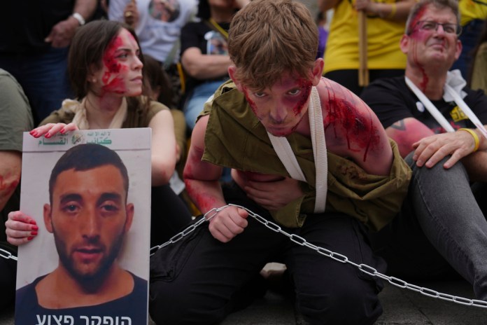 Ofir Angrest, center, wears fake blood and theatrical makeup at a demonstration calling for the release of his brother, Israeli soldier Matan Angrest, who was abducted by Hamas militants at Kibbutz Nahal Oz on Oct. 7, 2023, in Tel Aviv, Israel, Monday, April 21, 2025. (AP Photo/Ariel Schalit)