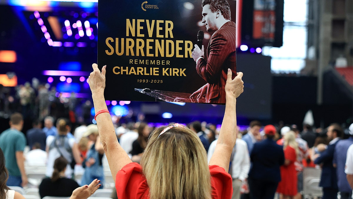A woman holds up a sign honoring Charlie Kirk at his memorial in Arizona.