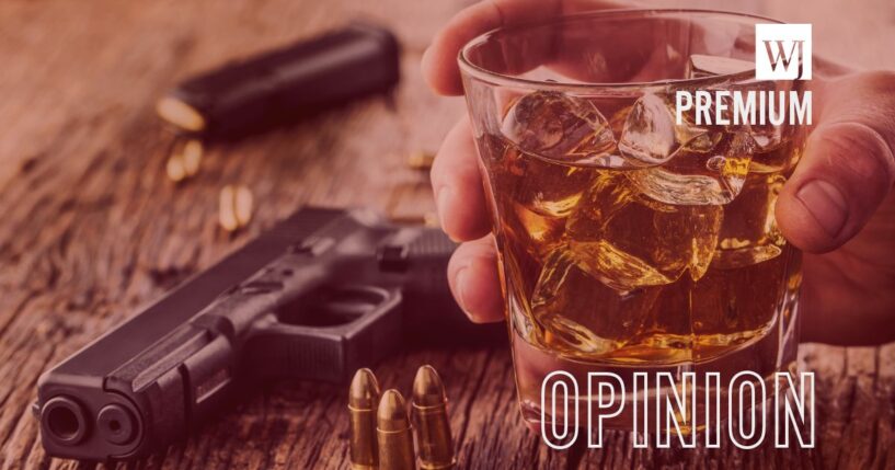 A 9mm pistol gun next to a cup of whiskey.