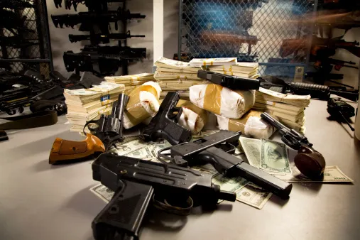 A pile of guns, drugs, and money on a table.