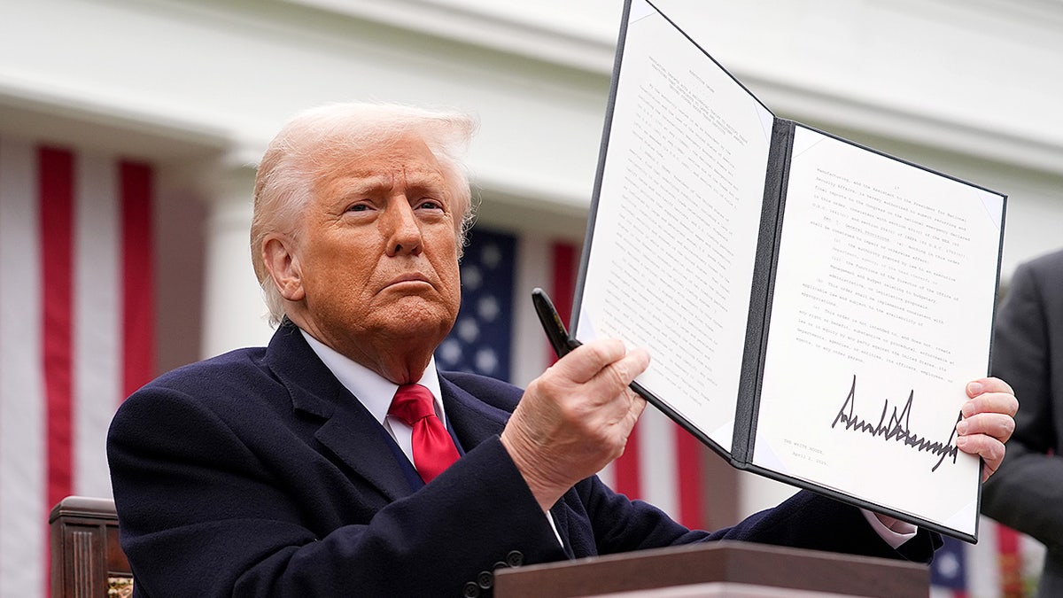 President Donald Trump holds up a signed executive order imposing tariffs during a Rose Garden trade announcement.