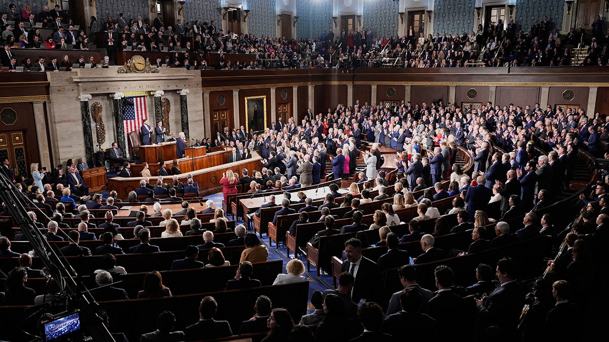 Donald Trump standing at a podium and speaking during the State of the Union address in the House chamber.