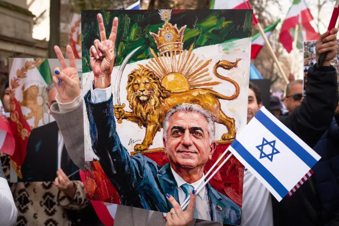 A member of the Iranian community flashes a victory sign from behind a poster of Iran's exiled Crown Prince Reza Pahlavi.
