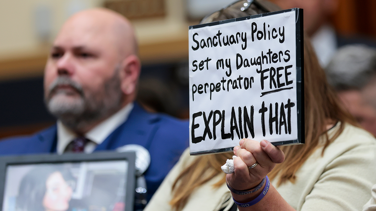 An attendee holds up a sign that reads "Sanctuary policy set my daughters perpetrator free, explain that"
