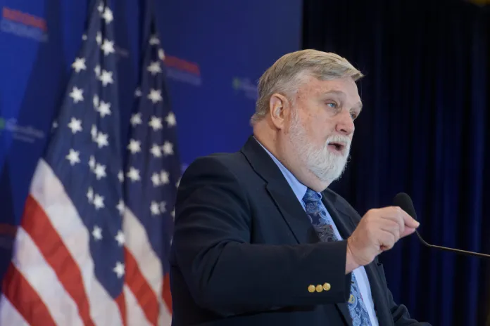Douglas Wilson speaks in front of a pair of American flags
