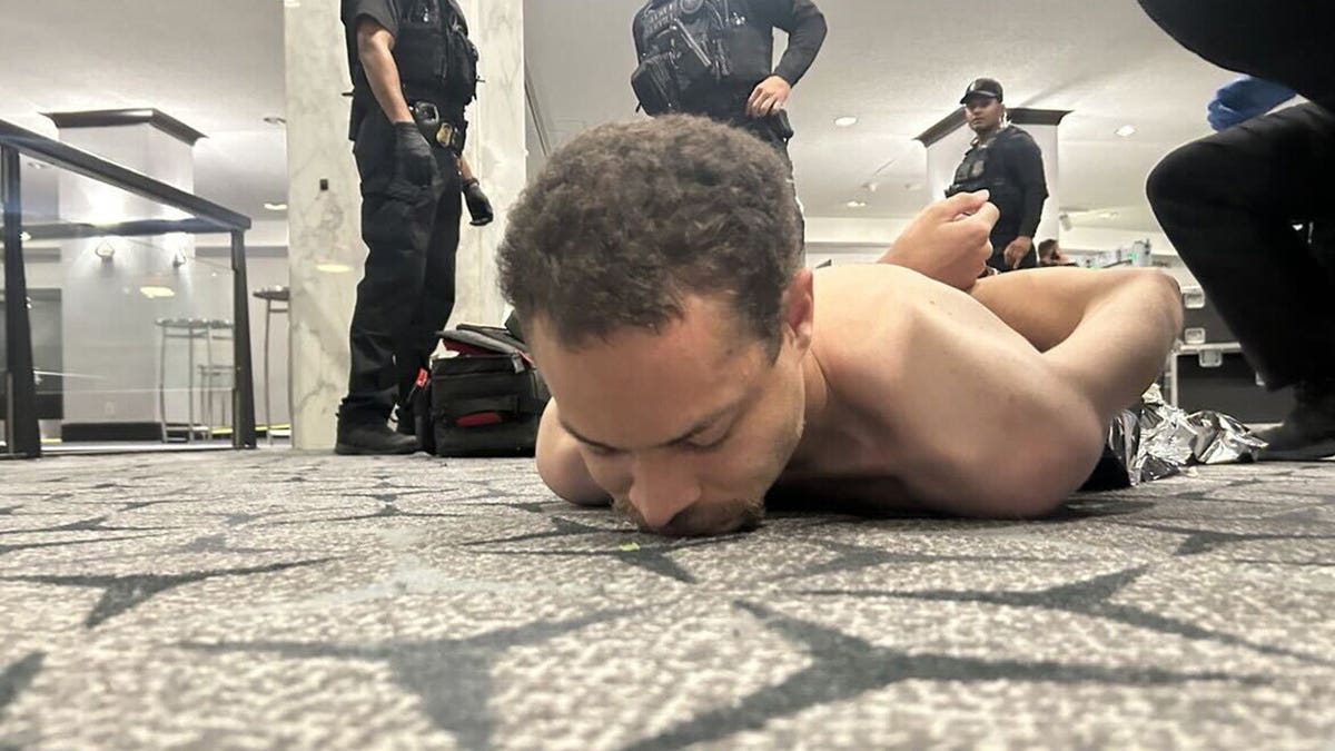 Cole Allen lying face down on the floor while law enforcement officers detain him