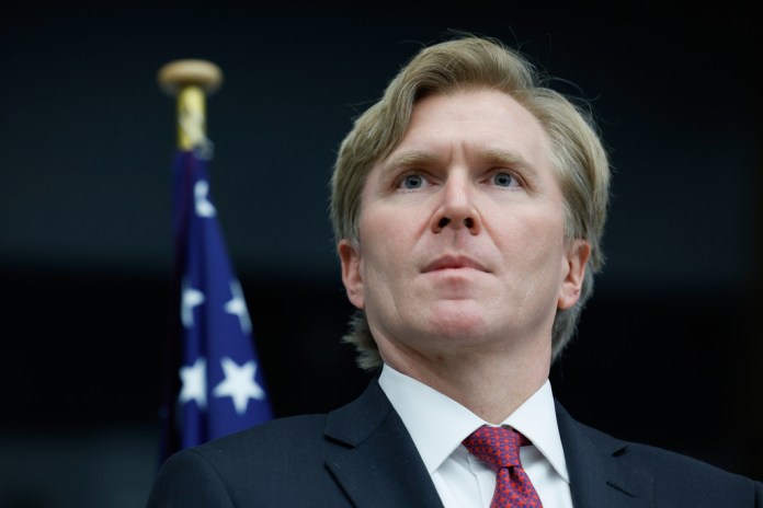 Elbridge Colby stands in front of an American flag