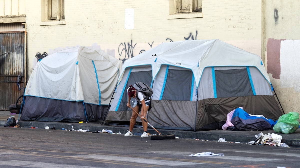 A homeless person clearing rubbish at a homeless camp on a sidewalk in Los Angeles