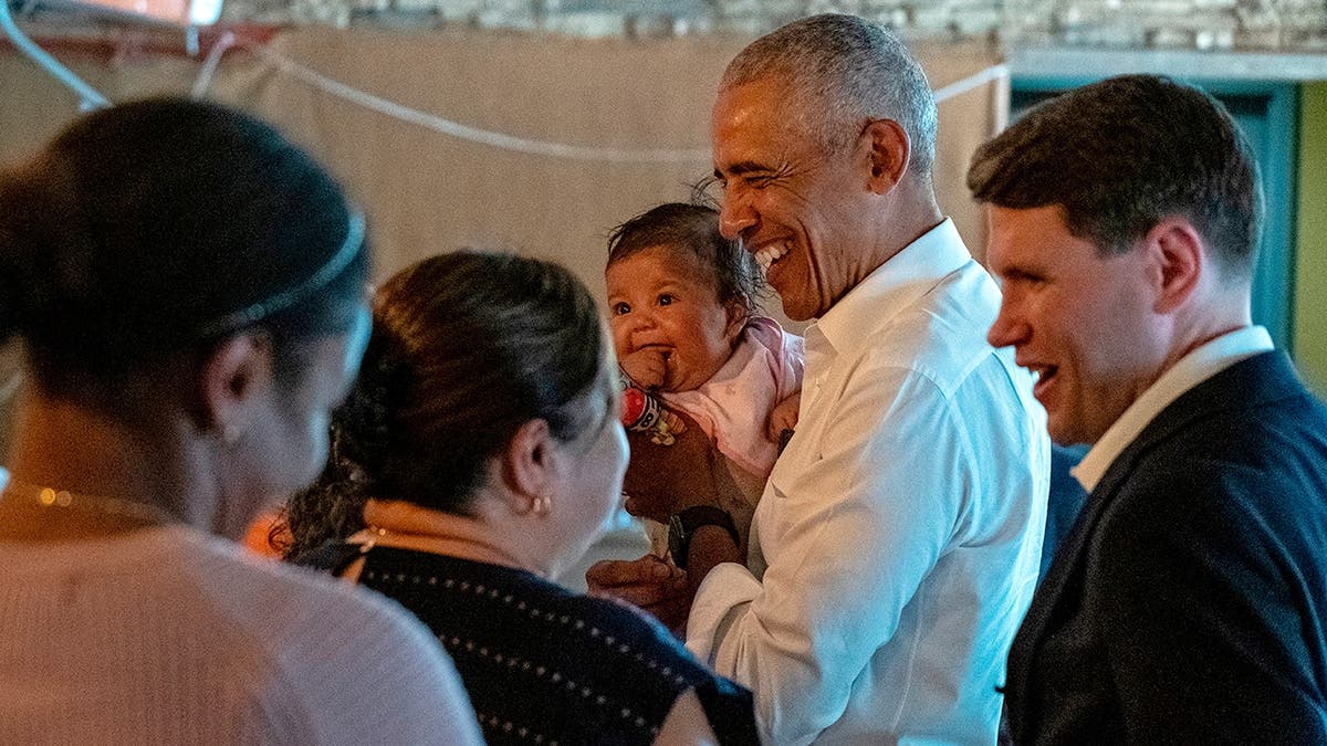 Barack Obama and James Talarico standing inside a restaurant and talking to patrons at a table.