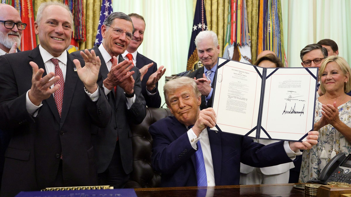 President Donald Trump displays signed Secure America Act in Oval Office as members of Congress applaud