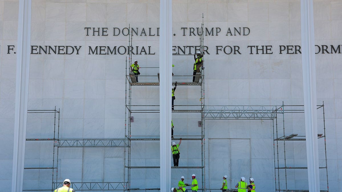 Construction workers building scaffolding near the Donald J. Trump and John F. Kennedy Memorial Center sign in Washington, D.C.