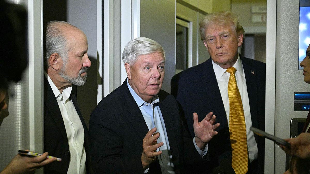 Lindsey Graham speaks with reporters aboard Air Force One with Donald Trump and Howard Lutnick nearby.