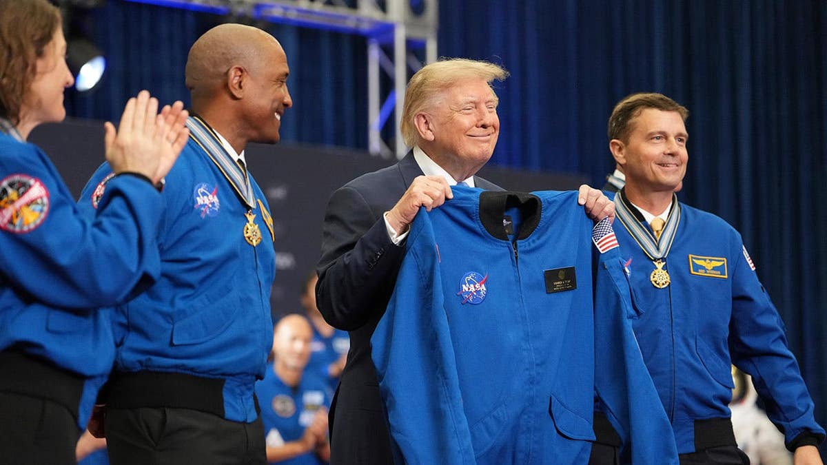 President Donald Trump holds up a flight jacket with Artemis II crew members Christina Koch, Victor Glover, Reid Wiseman and Jeremy Hansen.