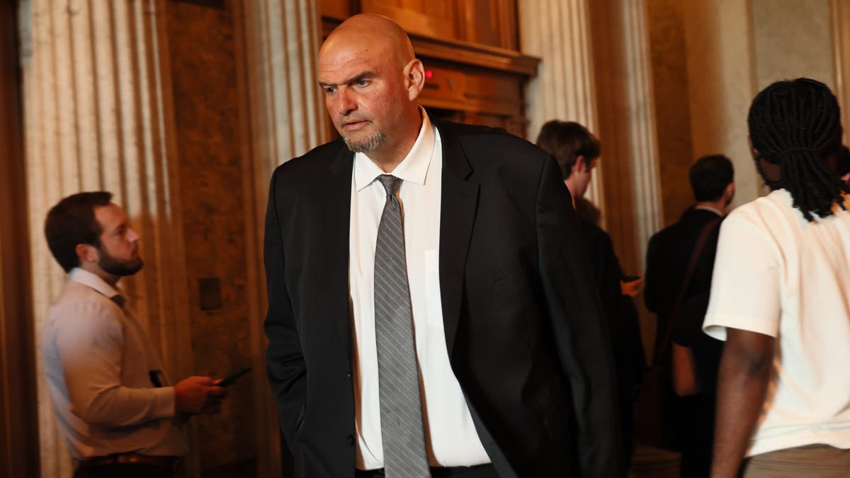 john fetterman pictured in a black suit and tie in a government building