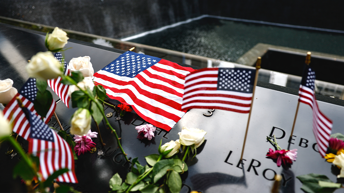 Flowers and American flags rest at 9/11 Memorial reflecting pool.