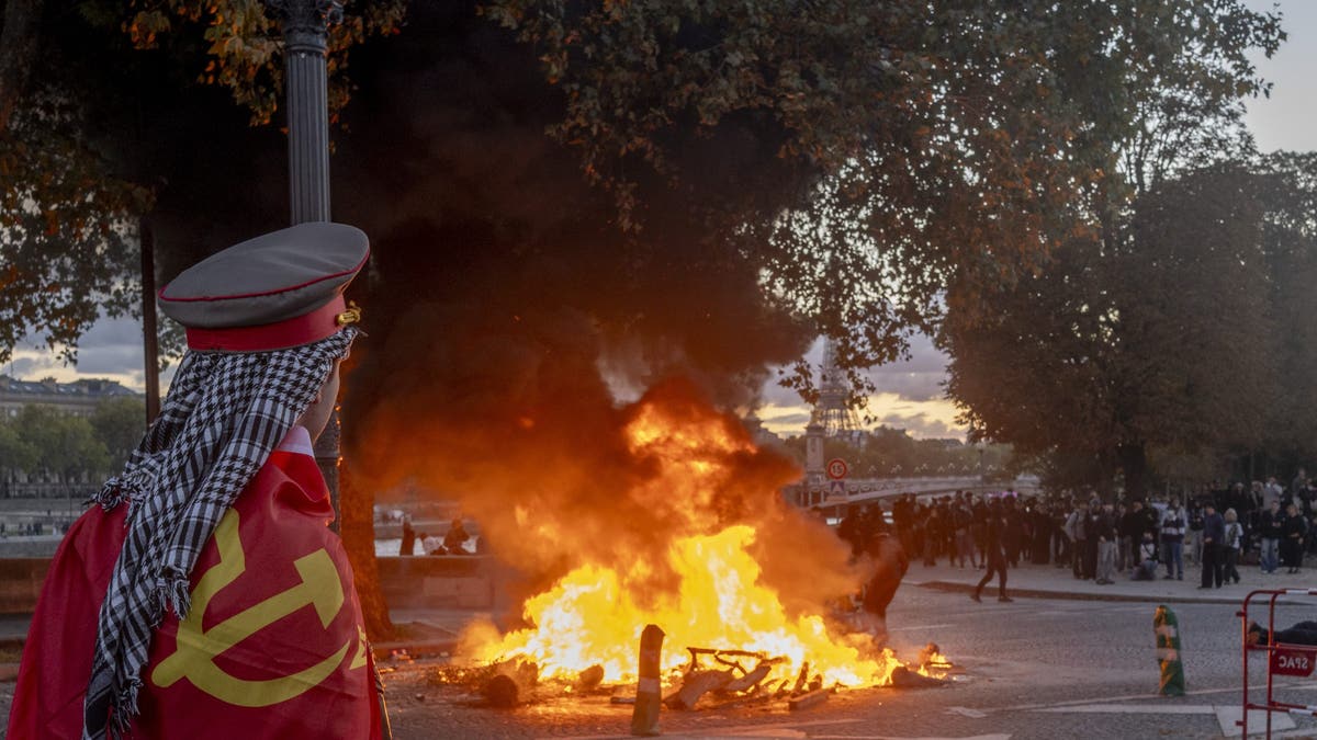 A protester watches a fire burn at a demonstration in Paris, France, on Saturday, Oct. 17, 2026. Rioters attacked French public buildings and looted stores in cities including Paris as protests against the high cost of living drew more than half a million people, underscoring the nation's challenges ahead of presidential elections next year. Photographer: Nathan Laine/Bloomberg via Getty Images