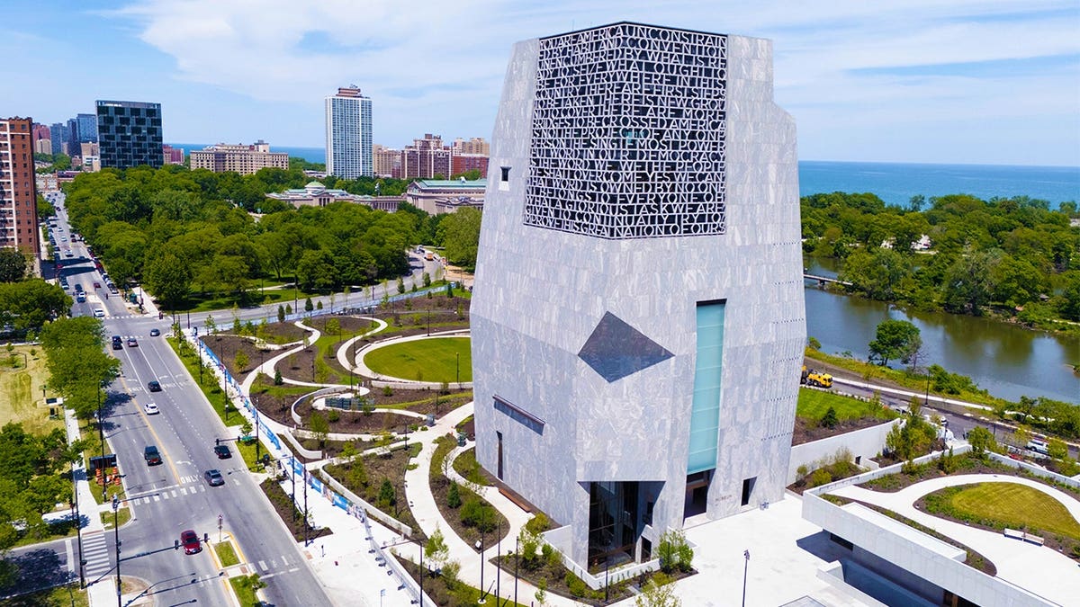 Aerial view of the Obama Presidential Center's tall stone museum tower, landscaped grounds and surrounding roads in Chicago.